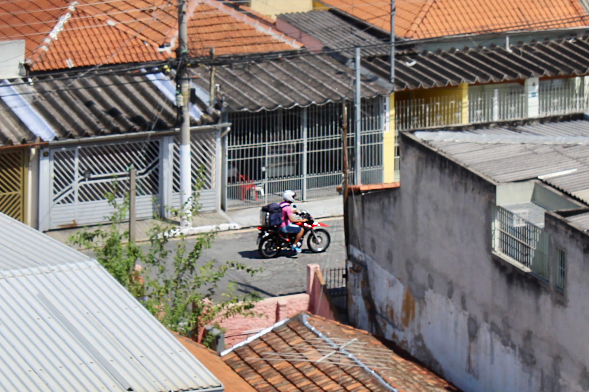 App delivery worker riding a motorcycle at speed, insulated backpack on his back, on a Brazilian street